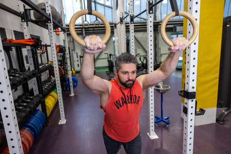 Fit man pulling up on gymnastic rings in gym, training, training his biceps and triceps.