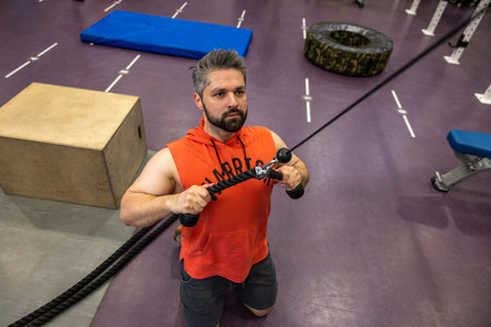 Strong sporty man training triceps and biceps at gym, doing cable rope pushdowns.