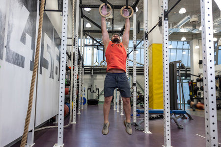 Fit man pulling up on gymnastic rings in gym, training, training his biceps and triceps.
