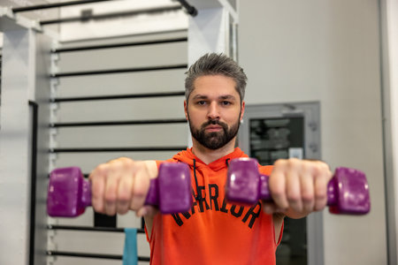 Athletic man working on his biceps and triceps lifting dumbbells training arms in the gym.