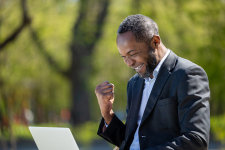 African american businessman working on laptop in the park and looking contentedの写真素材