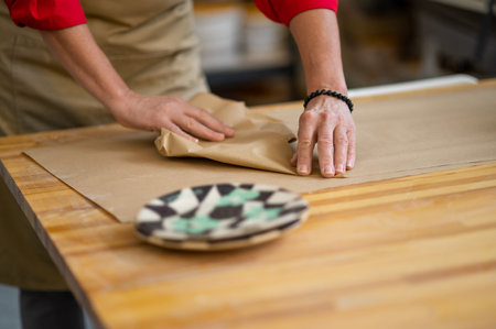 Hands of woman pottery master wrapping earthenware item ordered by client into paper.の写真素材