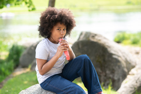 Little girl with curly hair eating delicious chocolate ice cream in garden and enjoys on hot day.の写真素材