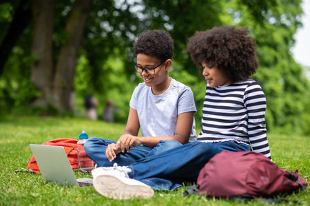 Two african american kids sitting on the grass in the parkの写真素材