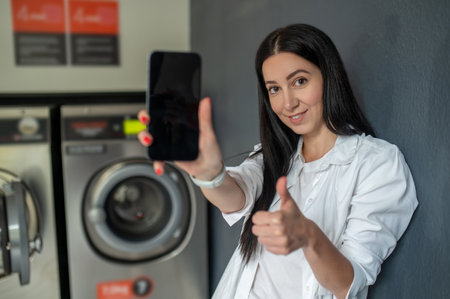 Woman waiting in a laundry room showing mobile phone with empty display copy space for advertisementの写真素材