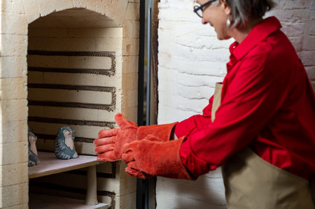 Mature craftswoman taking clay products from pottery kilnの写真素材
