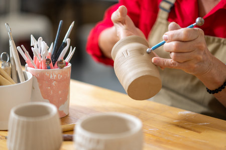 Unrecognizable woman painting on earthenware in pottery workshop, decorating clay products.の写真素材