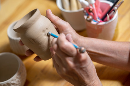 Unrecognizable woman painting on earthenware in pottery workshop, decorating clay products.の写真素材