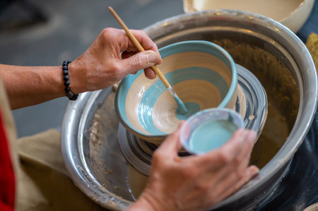 Closeup of woman painting clay mug, coloring pottery in workshop with a paintbrush.の写真素材