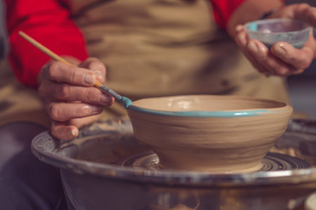 Closeup of woman painting clay mug, coloring pottery in workshop with a paintbrush.の写真素材