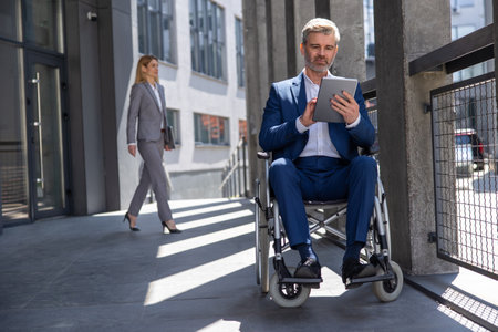 Executive business man in wheelchair with tablet using mobile device for work outdoors.の写真素材