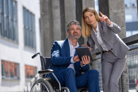 Woman and man in wheelchair working together, joint architecture project, using laptop and tablet.の写真素材