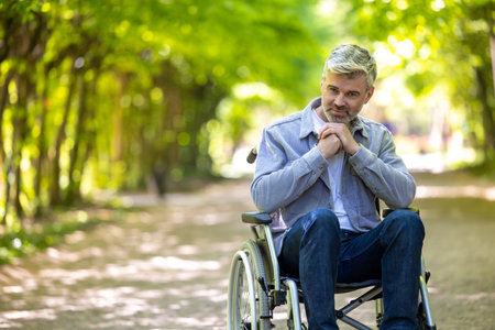 Disable man wearing casual clothing spending time in summer park riding wheelchair.の写真素材