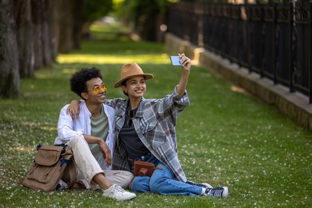 Cute couple sitting on the grass in the park and making selfieの写真素材