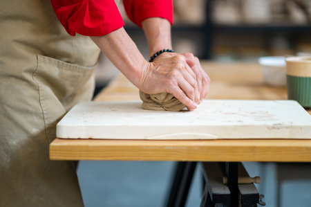 Unrecognizable woman wedging clay with hands standing behind table in studio.の写真素材