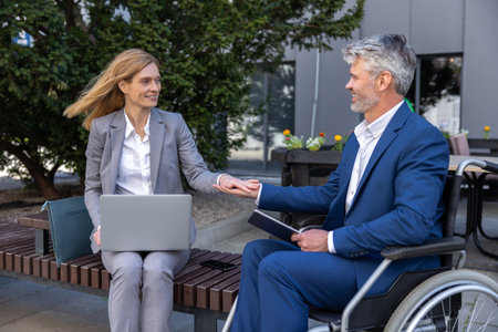 Two business persons holding hands and negotiating, colleague support, man in wheelchair.の写真素材