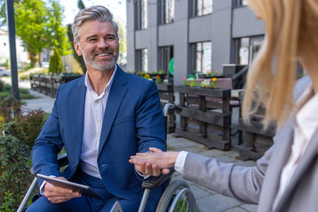 Two business persons holding hands and negotiating, colleague support, man in wheelchair.