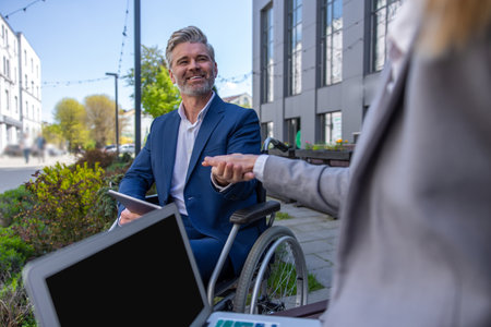 Two business persons holding hands and negotiating, colleague support, man in wheelchair.の写真素材