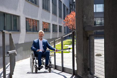 Gray haired businessman in formal wear gets to work in wheelchair rides ramp.の写真素材