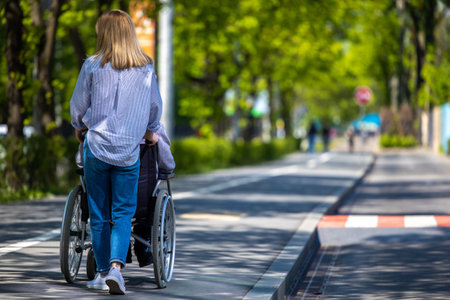 Husband in wheelchair and loving wife walking in city street.の写真素材