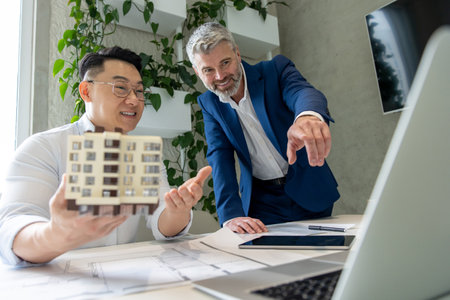 Architects in office using laptop and working on blueprint modeling new house together.の写真素材