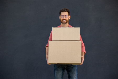 Dark-haired young man in eyeglasses carrying carton boxesの写真素材