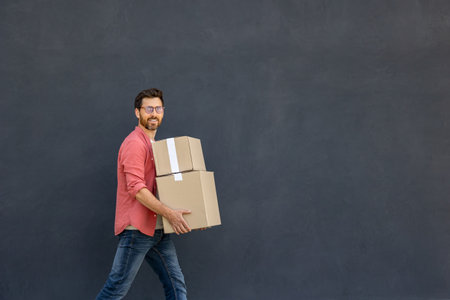 Dark-haired young man in eyeglasses carrying carton boxesの写真素材