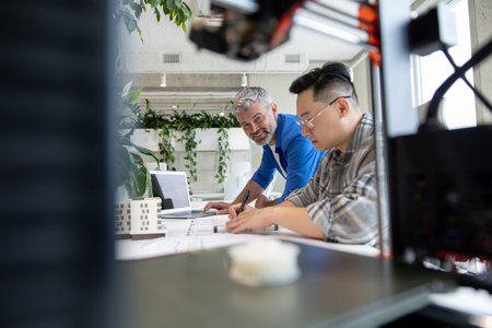 Two men architects using 3D printer in office and projecting house, drawing blueprints.