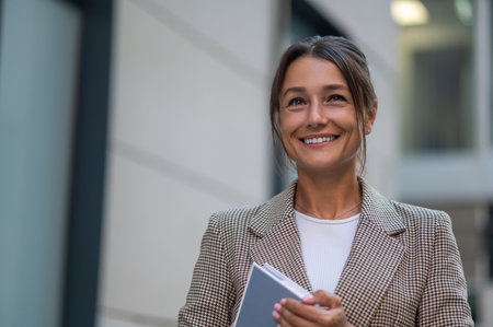 Happy woman holding her planner or book, wearing beige jacket.の写真素材