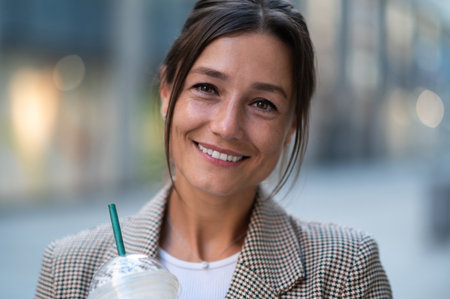 Woman drinking cocktail with straw posing against blurred city background.