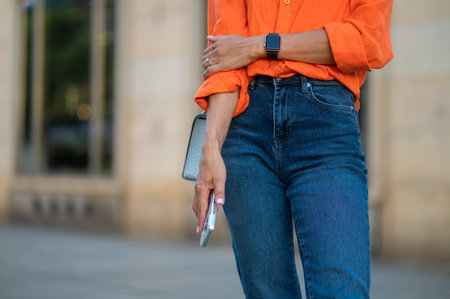 Unrecognizable woman standing outdoor with smartphone in hands.