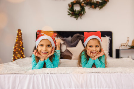 Adorable twins in christmas hats playing in bedの写真素材