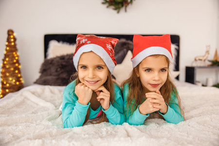 Adorable twins in christmas hats playing in bedの写真素材