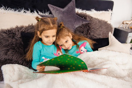 Two sweet girls lying in bed and reading fairy-talesの写真素材