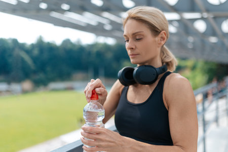 Woman drinking water from plastic bottle after running, resting after outdoor workout.