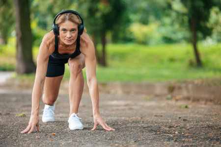 Woman in headphones standing in lower position before starting to run.