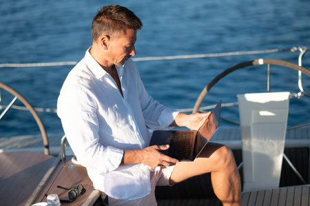 Successful mature man with a laptop working on a yachtの写真素材