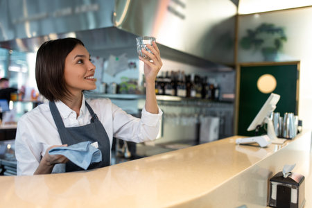 Dark-haired coffee shop assistant cleaning glasses and smiling