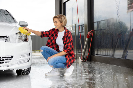 Blonde woman in checkered shirt washing a white carの写真素材