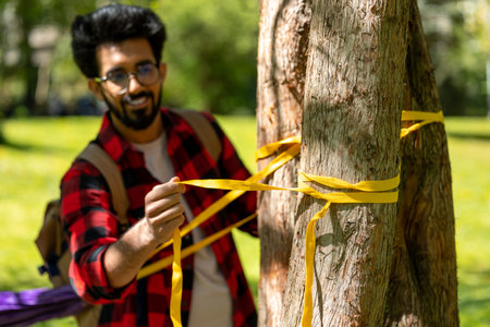 Man in checkered shirt tying ropes to the tree and adjusting hammockの写真素材