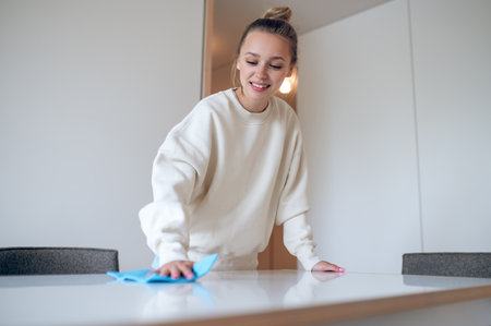 Woman housewife in white sweatshirt cleaning her home and wiping dust.