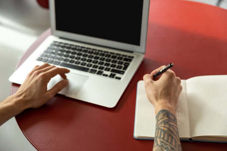 Close up picture of man working on laptop and making notes
