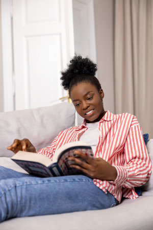 Smiling woman reading book while sitting on sofa at home.の写真素材