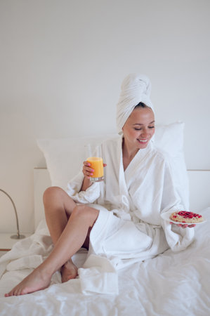 Cute young woman in bath robe having breakfast and feeling enjoyedの写真素材