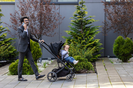 Elegant young man talking on the phone and carrying a baby carriage