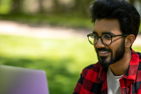 Dark-haired young man working on laptop in the park