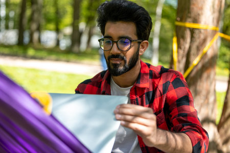 Bearded young brunette man working on laptop outdoors