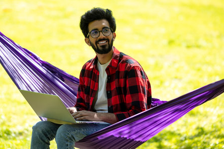 Contented bearded young hindu man with laptop in the park
