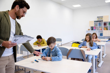 Male giving tasks on paper to pupils in classroom.