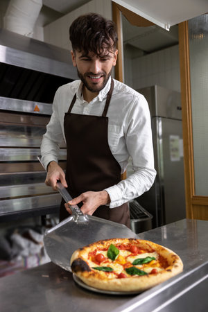 Dark-haired young man cooking pizza in pizzeriaの写真素材